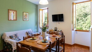 A cozy dining area with a wooden table set for four, surrounded by chairs. A television is mounted on the wall above the table. - Nonna Lena by Interhome (Molini di Prelà)