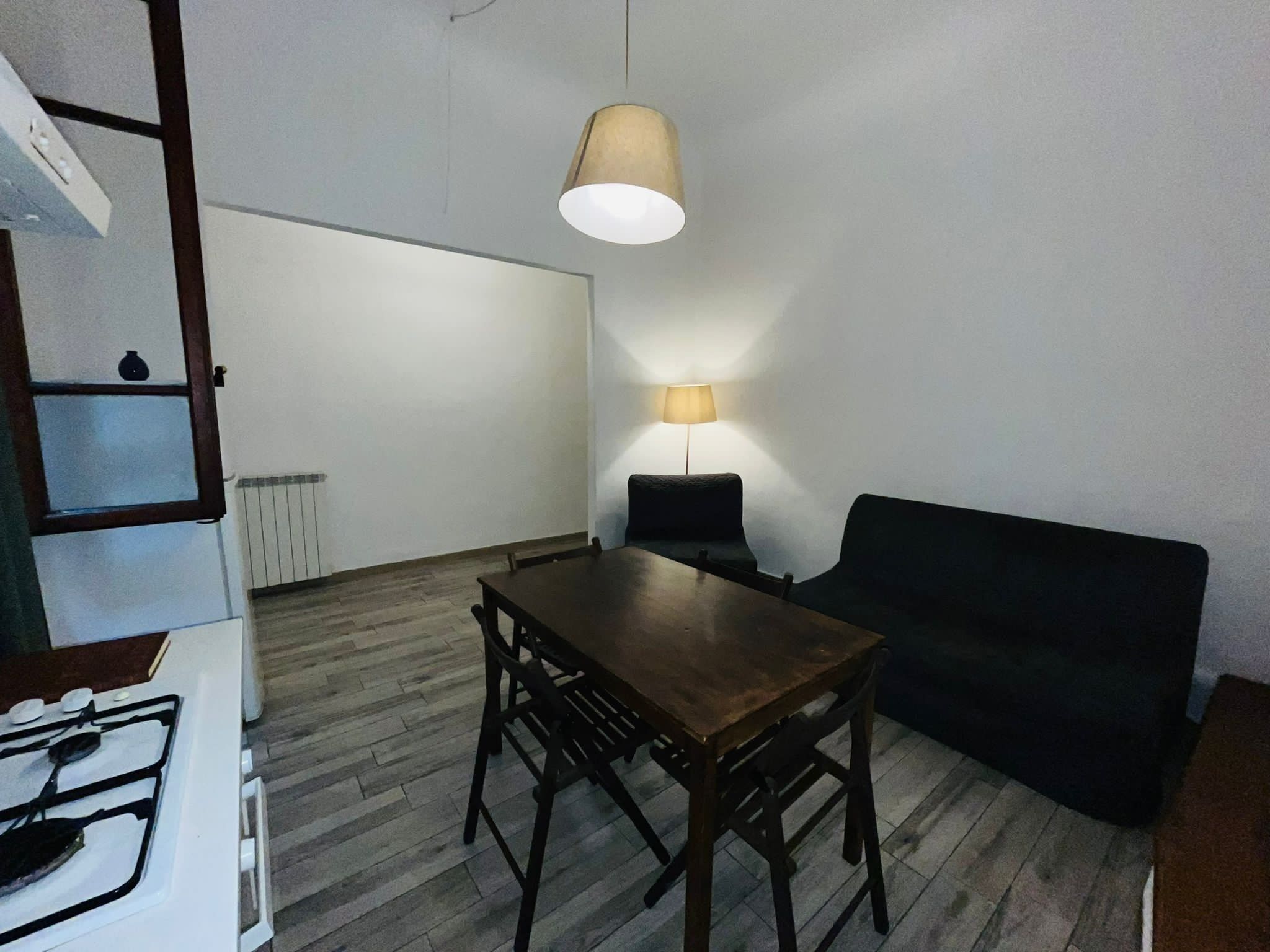 A compact living space with a dining table and chairs, a sofa, a lamp, and a stove.