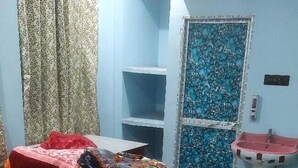 Een slaapkamer met een bed, een kussen, een rode deken, een wandairconditioner, een wastafel en een deur met een bloemendesign.