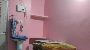 Een slaapkamer met roze muren, een bed met een deken in groen en geel, een nachtkastje met een lamp en een raam met een gordijn.