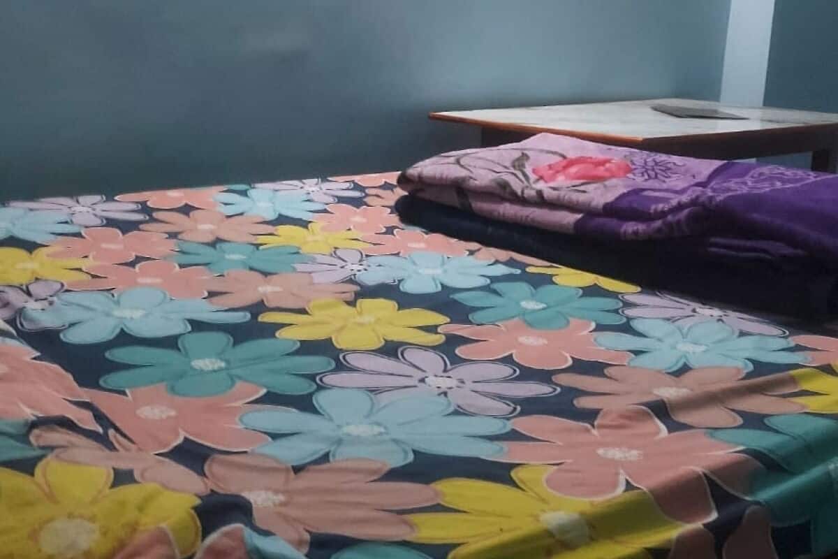 A room with a bed covered in a floral-patterned bedspread, a purple blanket, and a wooden headboard.