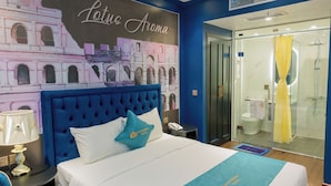 A hotel room with a large bed, a nightstand, a lamp, a wall mural, a bathroom with a glass shower, and a yellow curtain. - Lotus Aroma (Hanoi)