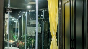 A bathroom with a glass partition, a yellow shower curtain, a sink, and a towel rack. - Lotus Aroma (Hanoi)
