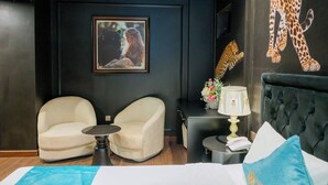 A modern hotel room with a large bed, two armchairs, a small table, a nightstand with a lamp, and a leopard print wall decoration. - Lotus Aroma (Hanoi)