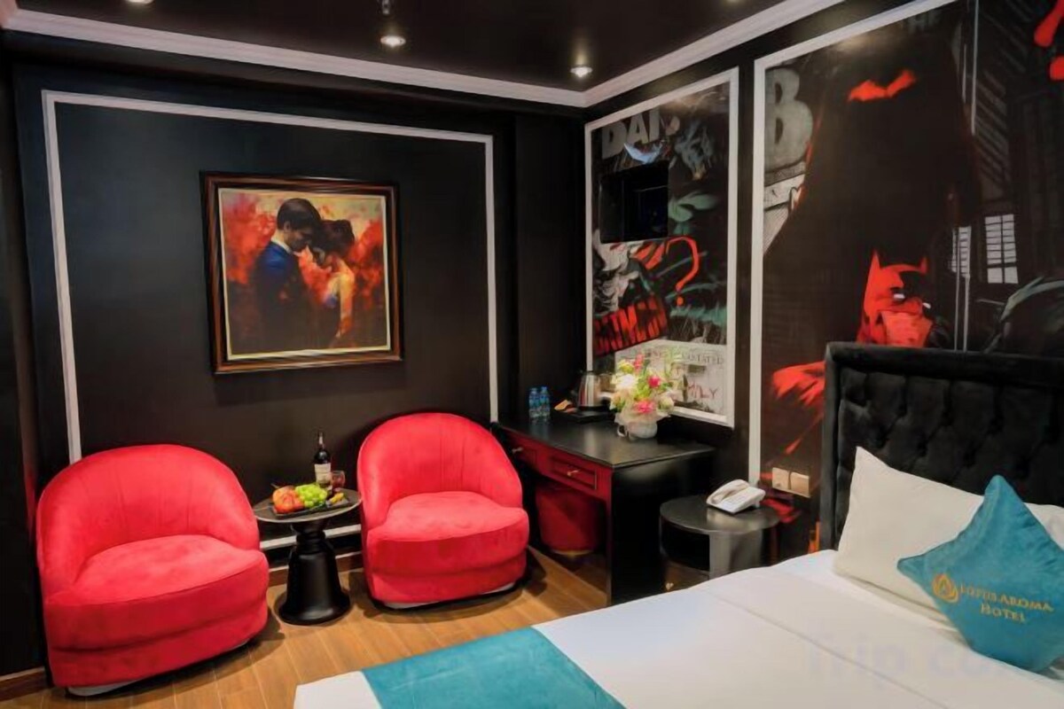 A hotel room with a bed, two red armchairs, a small table, and a wall with a large poster.