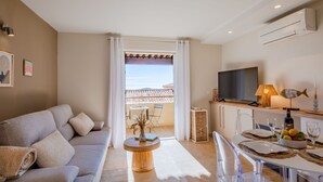 A modern living room with a sofa, a dining area with a table set for two, and a TV. - Le Bougainvillier by Interhome (Sainte Maxime)