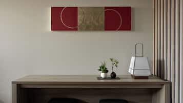 A modern desk with two black upholstered chairs, a small potted plant, and a lamp on a wooden table against a wall with a red and beige abstract painting.