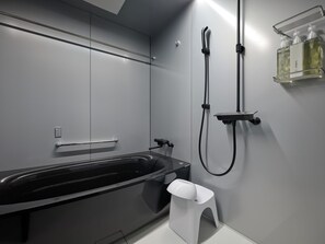 Un baño moderno con una bañera negra, un cabezal de ducha manual y un dispensador de jabón en la pared.