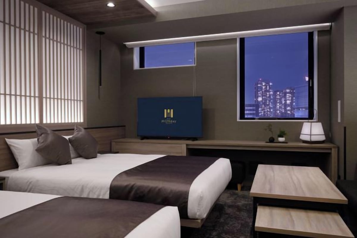 Een hotelkamer met twee bedden, een televisie, een bureau en een raam met uitzicht op de stad.