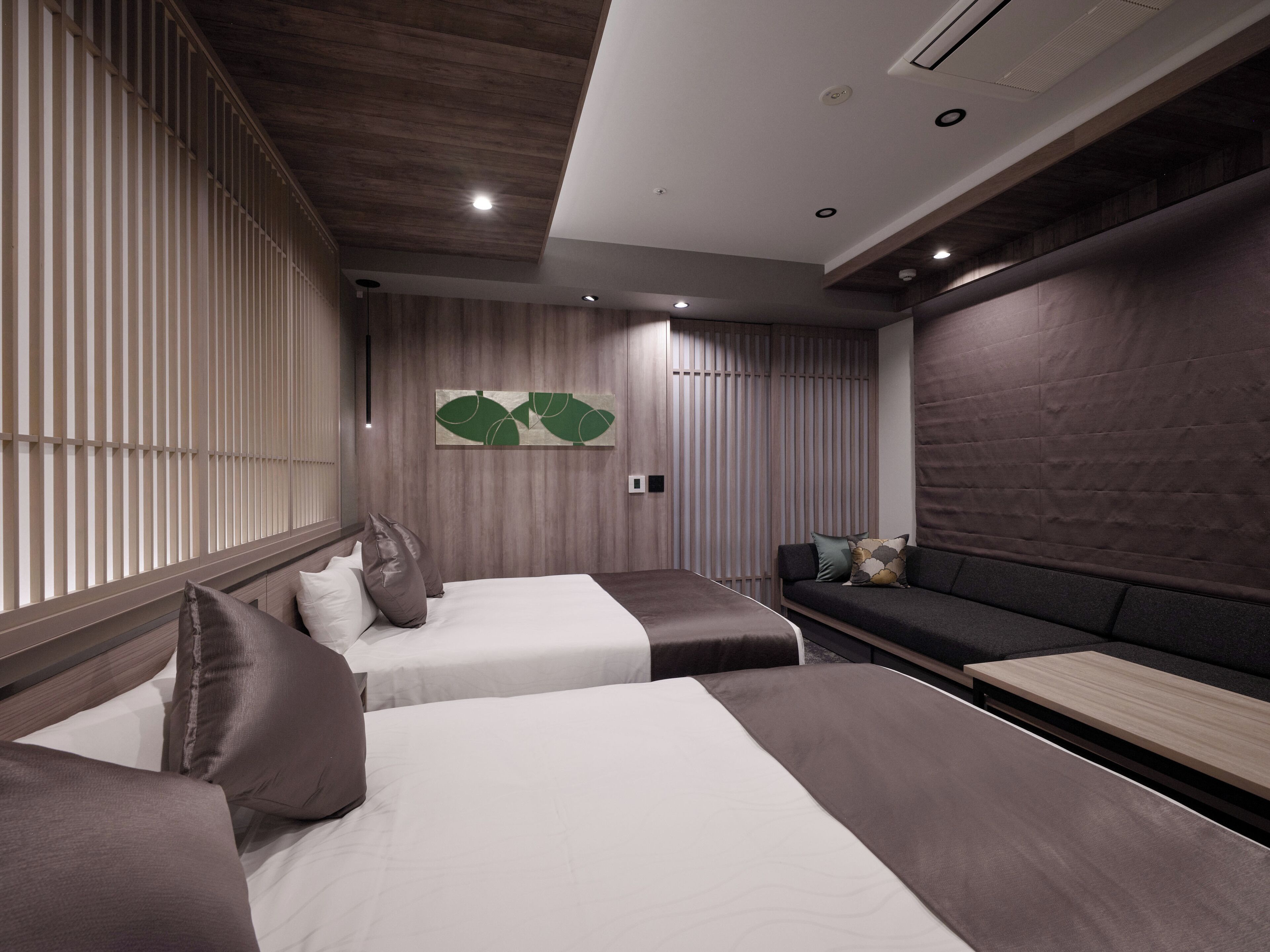 A modern hotel room with two beds, a sofa, and a wooden accent wall.
