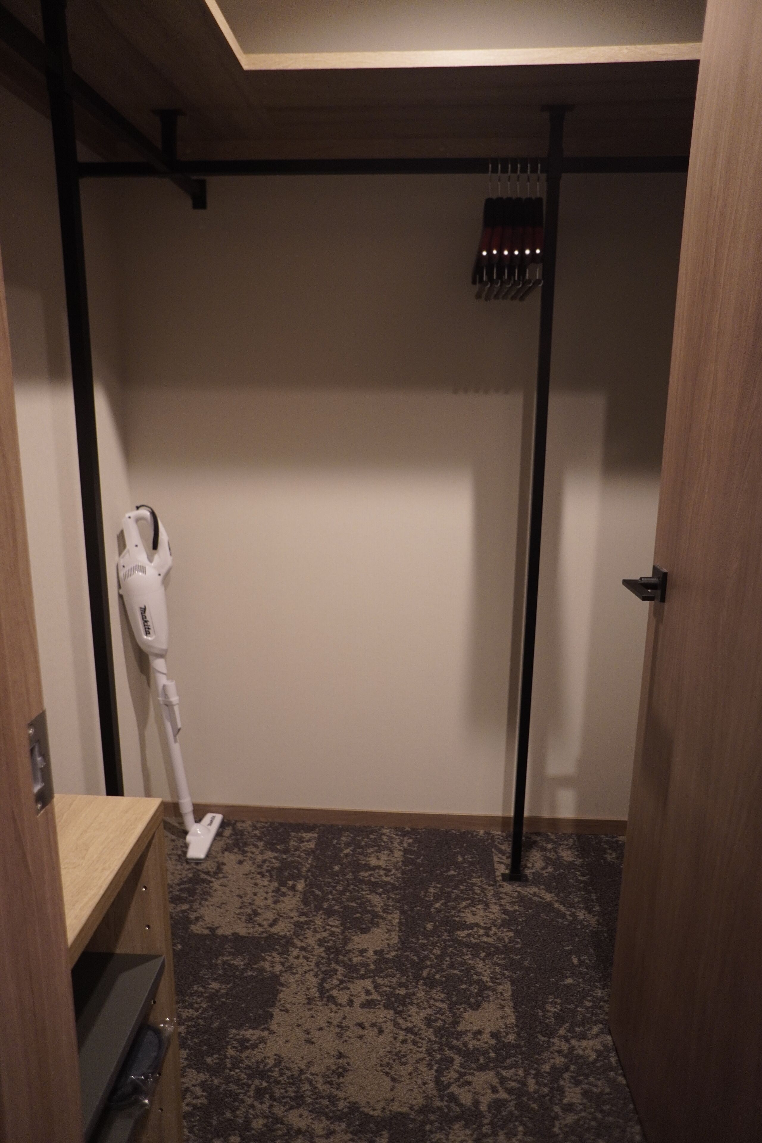 A room with a vacuum cleaner, a wooden shelf, and a door.