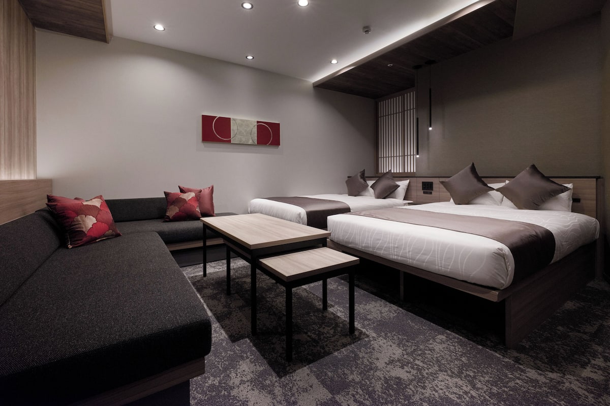 Habitación de hotel moderna con sofá, dos camas, una mesita y un techo con iluminación empotrada.