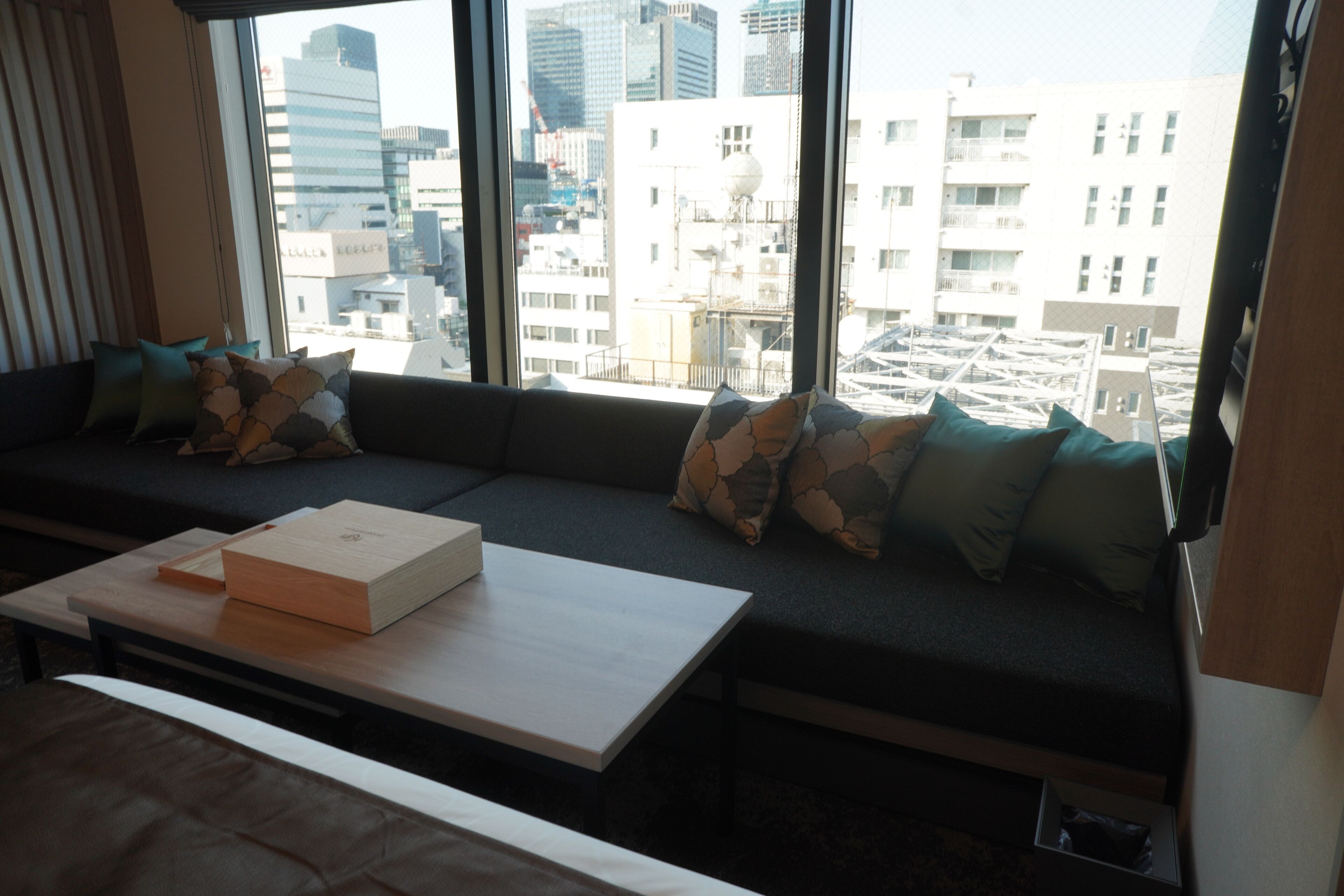 A modern room with a large window, a sofa with cushions, a wooden table, and a city view.