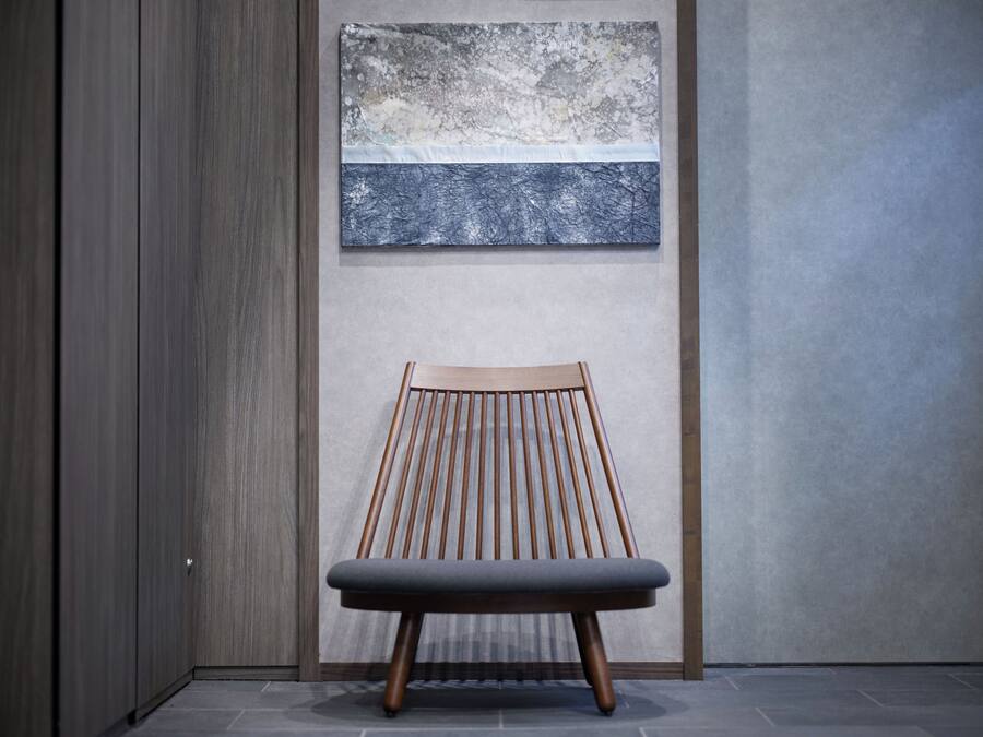 Ein modernes Interieur mit einem Holzstuhl und einem strukturierten Kunstwerk an der Wand.