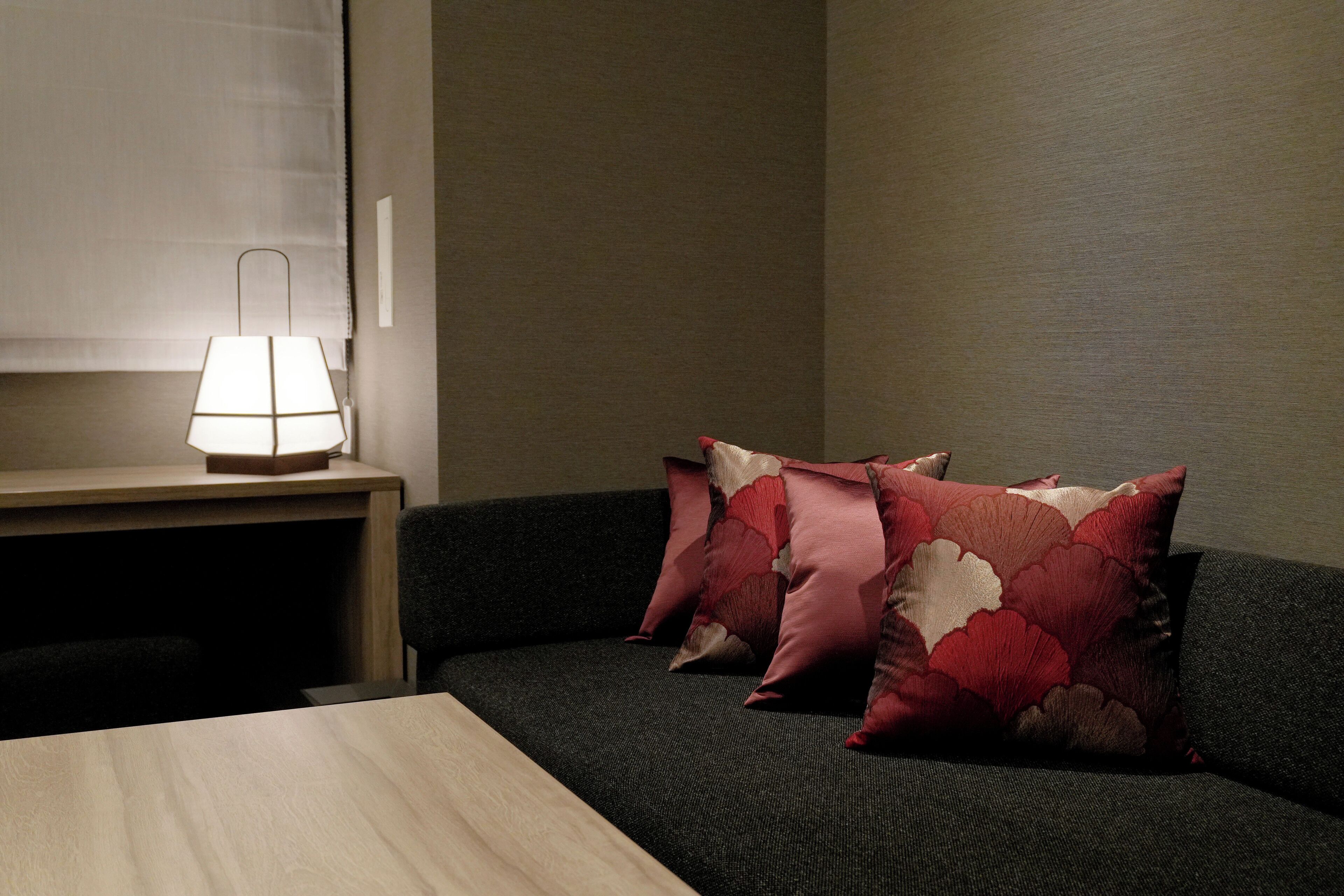 A room with a bed, a bedside table with a lamp, and two decorative pillows.
