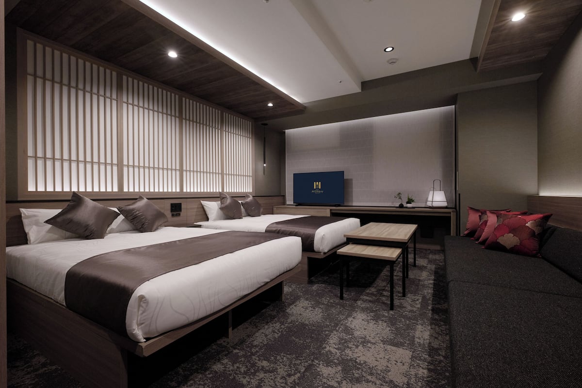 Una habitación de hotel moderna con dos camas, un sofá, una mesita y un televisor.