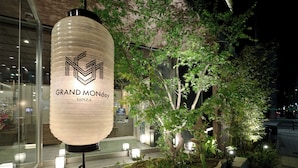 A well-lit outdoor area with a large hanging sign, a small tree, and a stone pathway. - GRAND MONday GINZA (Tokyo)