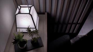 Una camera moderna con un muro a motivi geometrici, una lampada da terra nera e due piante in vaso su una superficie scura.