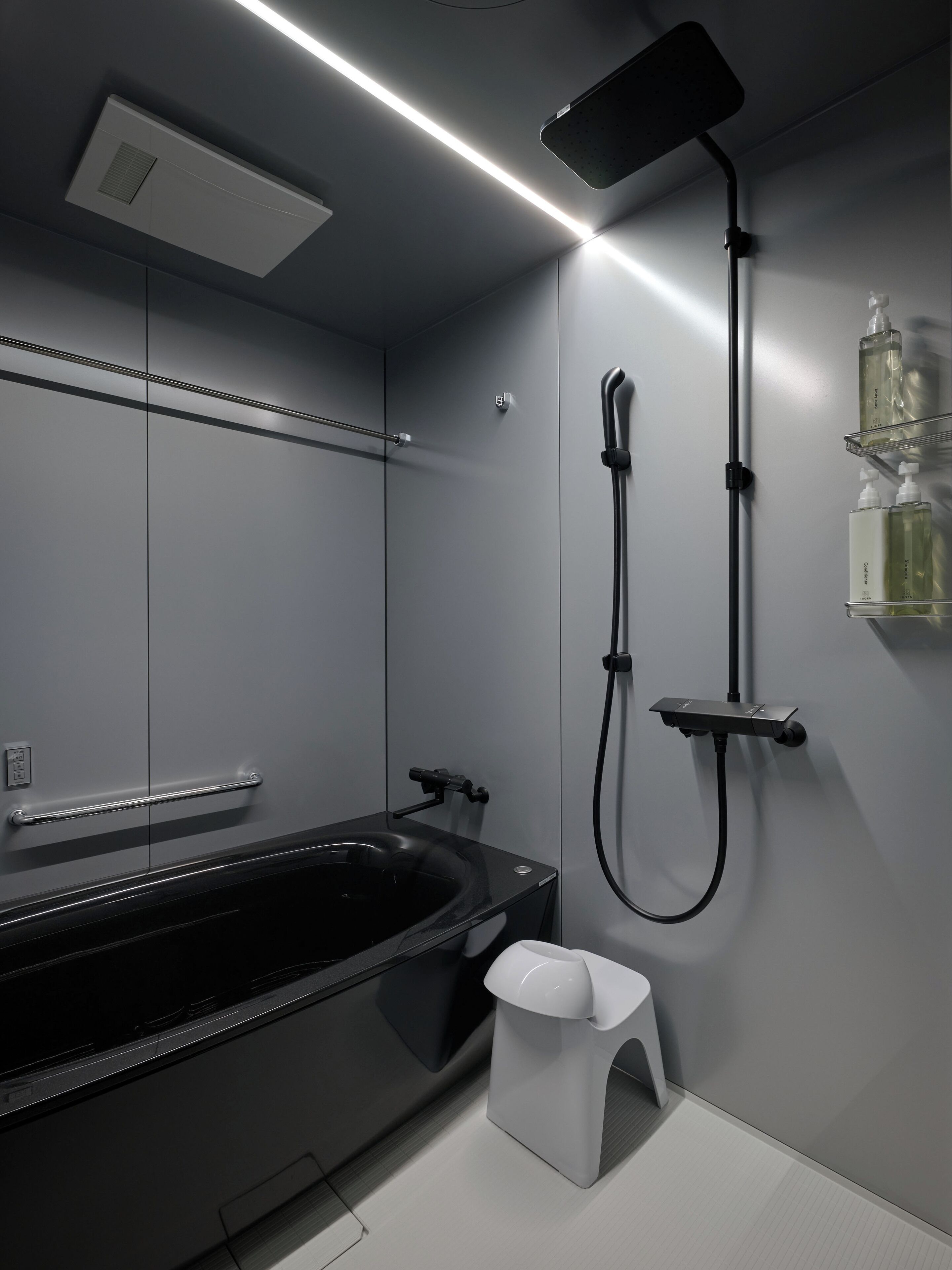 Une salle de bain moderne avec une baignoire noire, une douchette et un tabouret blanc.
