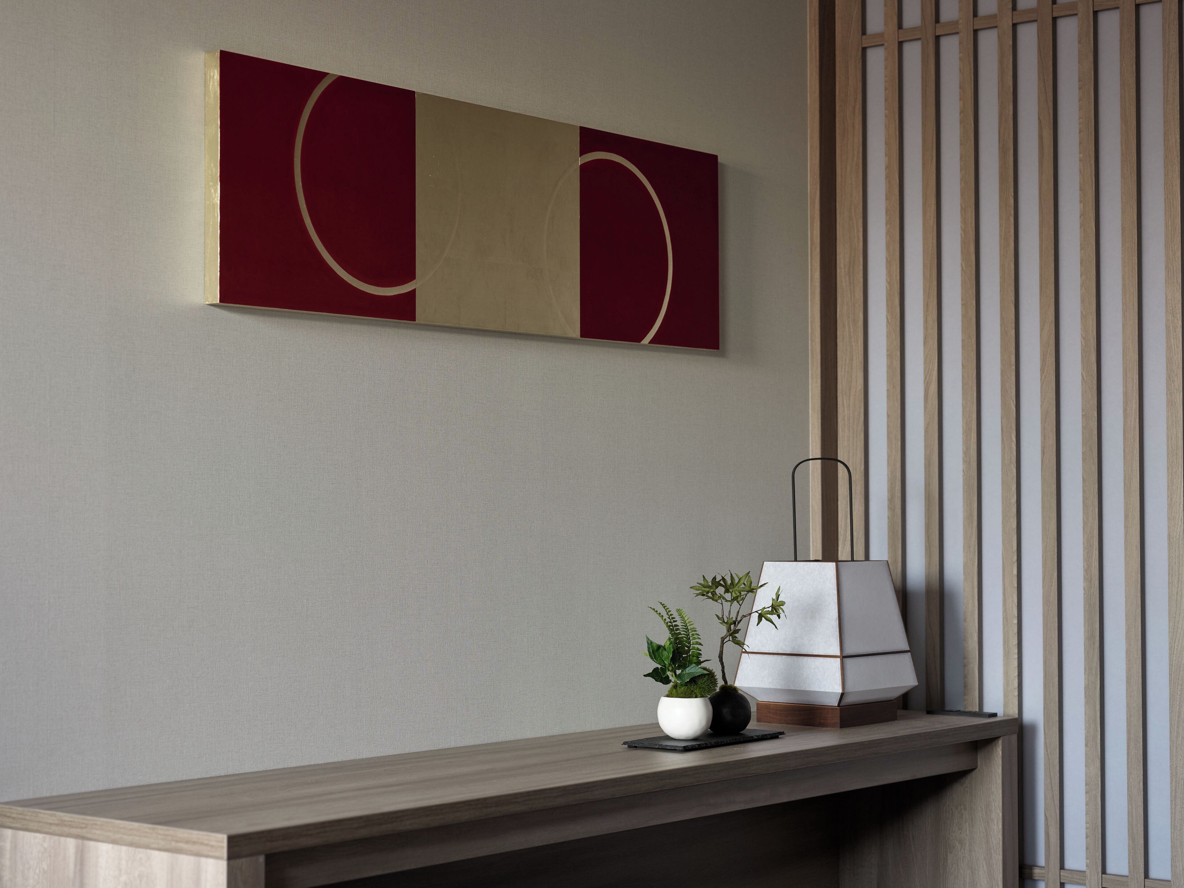 A minimalist room with a wooden desk, a potted plant, and a modern abstract painting.