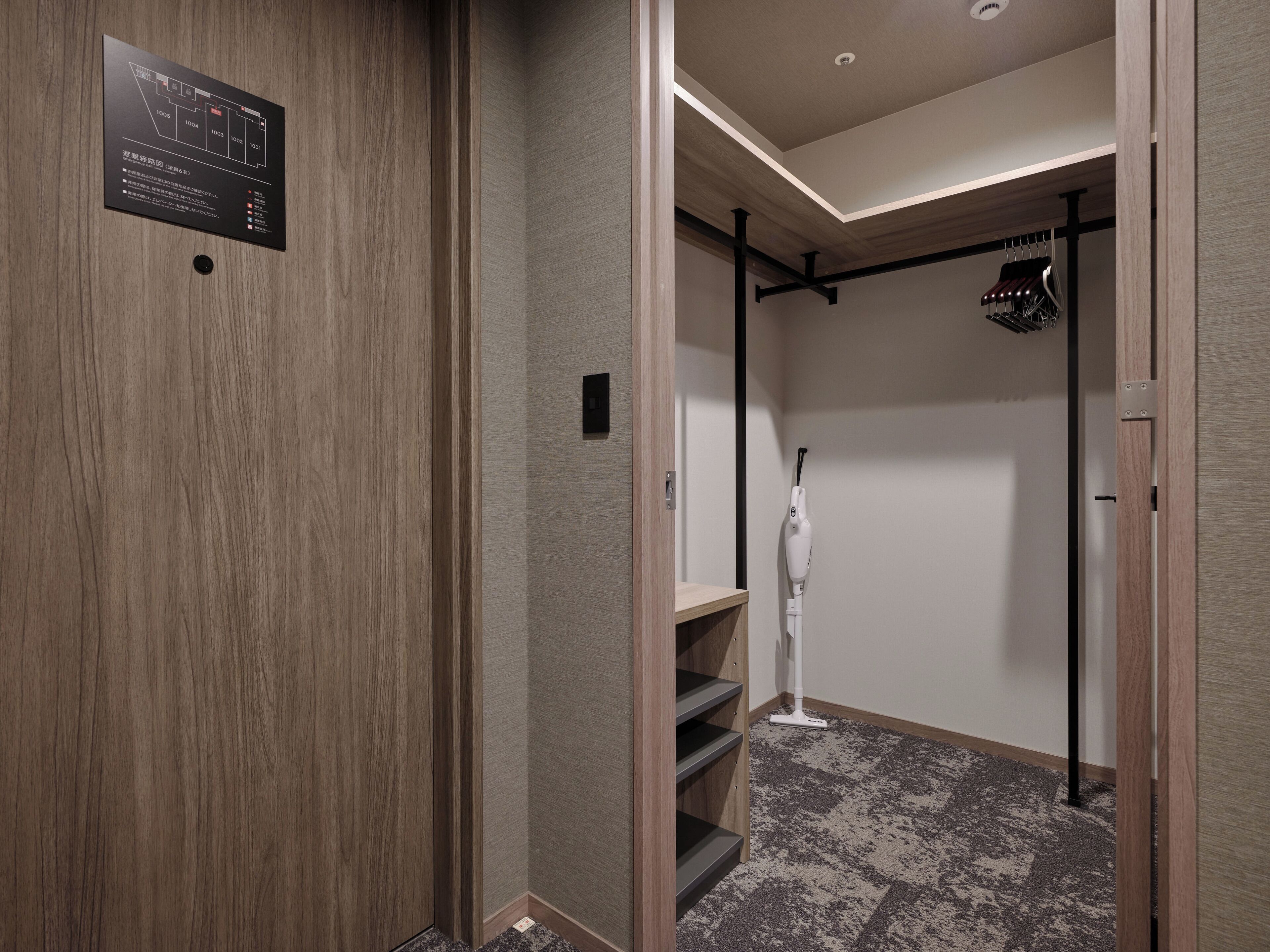 Quarto de hotel moderno com piso de madeira, área com carpete, suporte para sapatos e secador de sapatos fixado na parede.