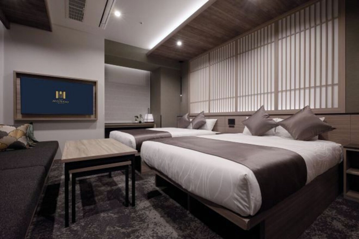 Una habitación de hotel moderna con dos camas, un sofá, una mesita y un ventanal grande con persianas verticales.