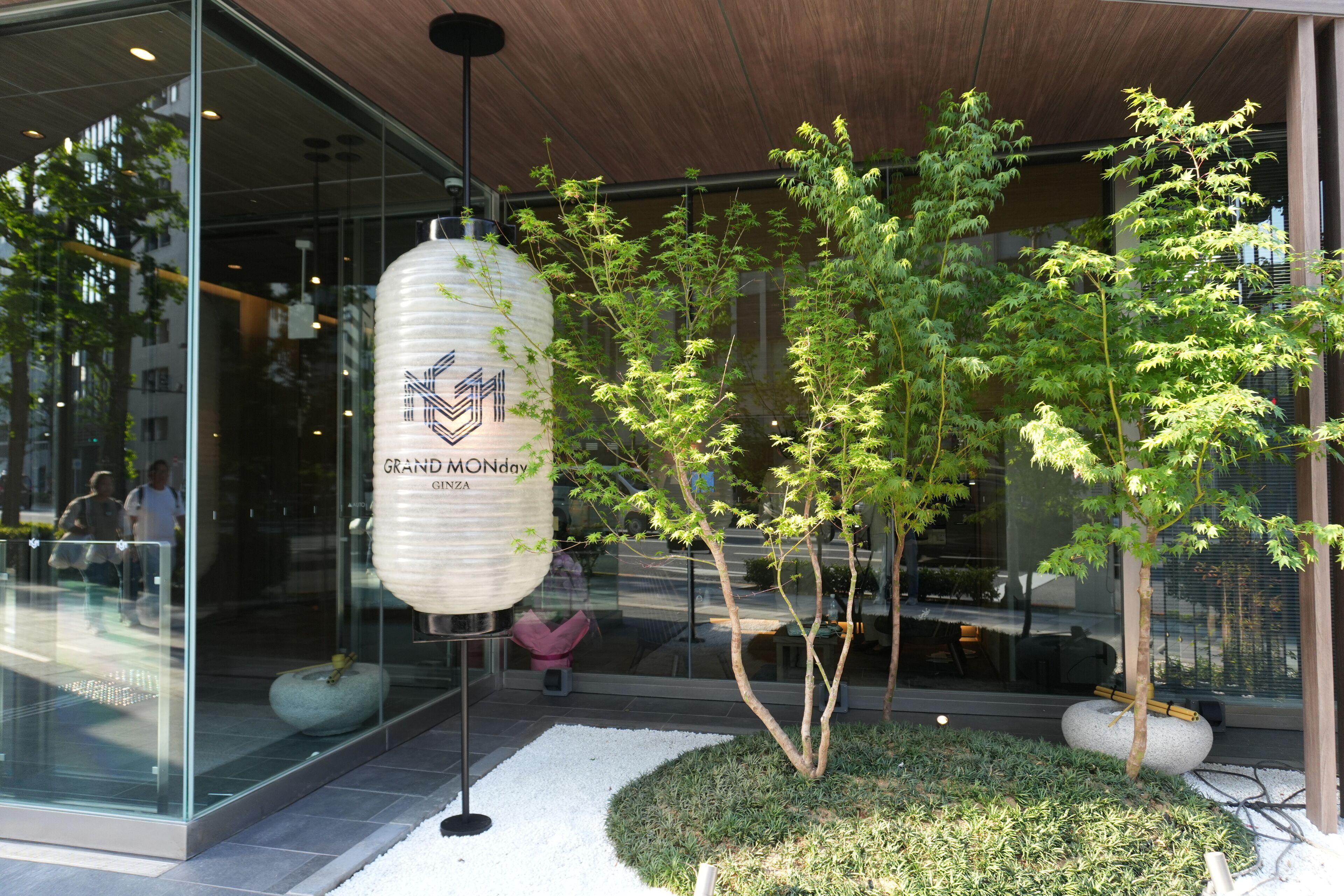 A modern building with glass windows, a hanging lantern, and a small tree in the foreground.