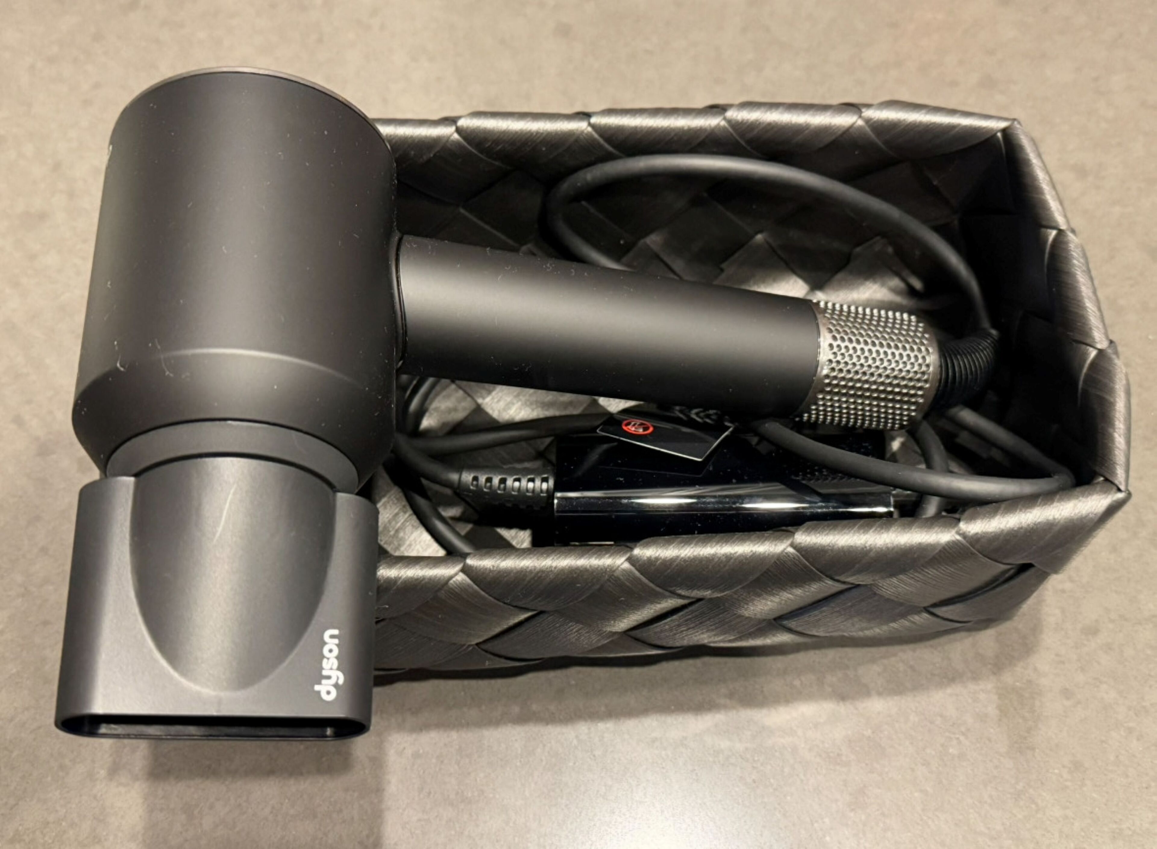 Een zwarte microfoon met een kabel en een stroomadapter in een gevlochten mand.
