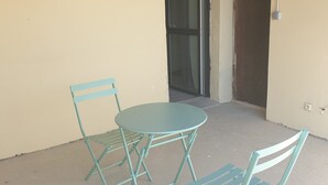 A small outdoor seating area with a round table and two chairs, a sliding glass door, and a concrete floor. - Furnished studio (Montaigu-Vendée)
