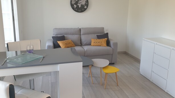 A modern living space with a grey sofa, two yellow stools, a small round table, and a world map clock on the wall. - Furnished studio (Montaigu-Vendée)