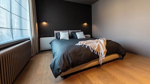 A modern bedroom with a large bed, a window with curtains, a wall-mounted light, and a radiator. - Villa Euphrosina (Ostend)