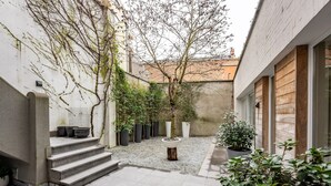A courtyard with steps leading to a seating area, surrounded by potted plants and a small table. - Villa Euphrosina (Ostend)
