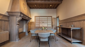 A dining area with a wooden table, six chairs, a wooden cabinet, and a fireplace. - Villa Euphrosina (Ostend)