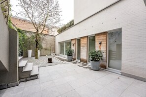 A modern courtyard with a minimalist design, featuring a seating area with benches, potted plants, and a gravel path. - Villa Euphrosina (Ostend)