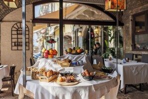 A breakfast buffet with various food items and a fruit bowl on a table in a restaurant with a rustic interior. - Hotel Alla Grotta (Lazise)
