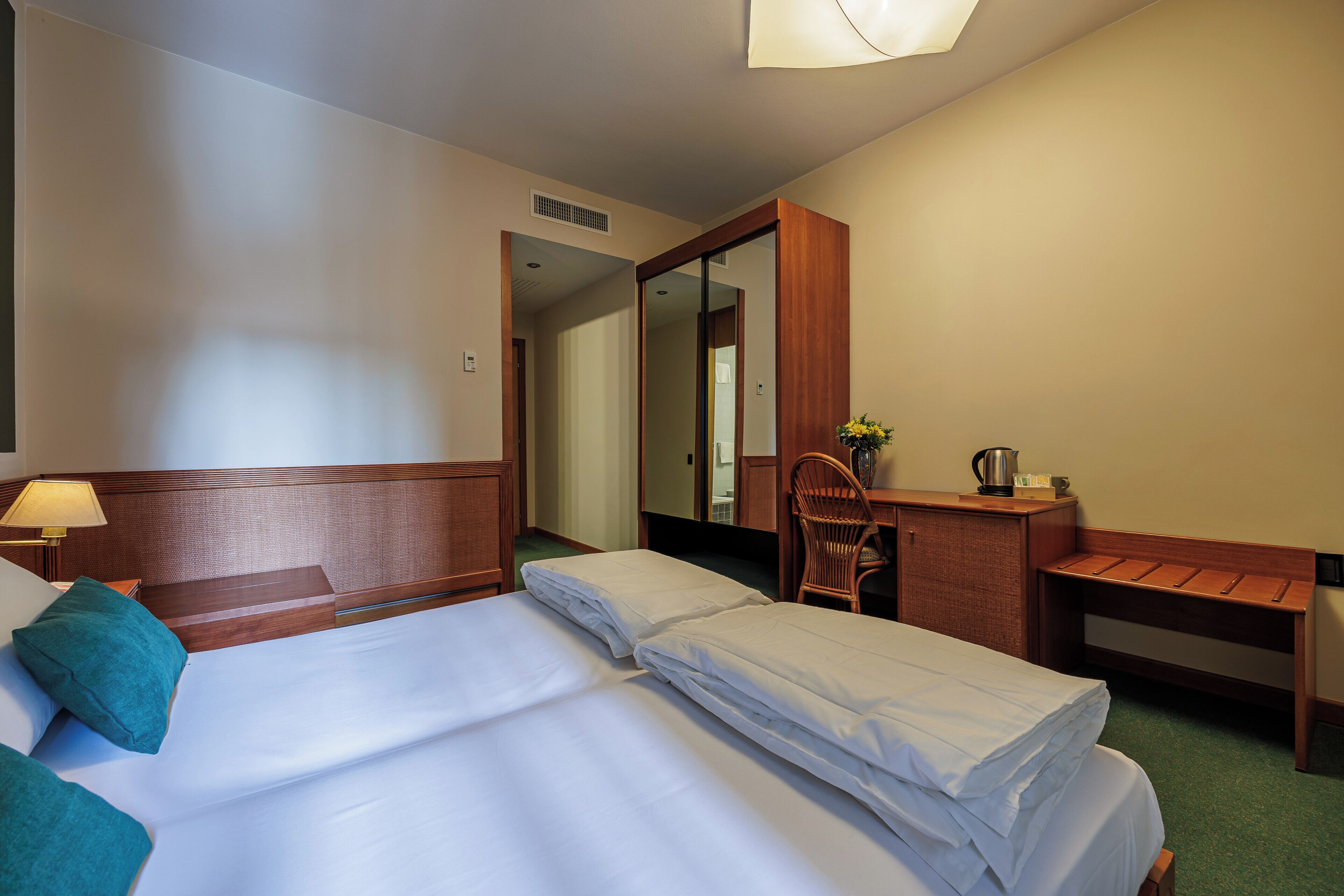 A hotel room with two beds, a desk, a chair, a mirror, and a lamp.