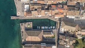 Vista aérea de un pueblo costero con un puerto deportivo, edificios escalonados y un paseo marítimo.