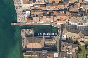 Una vista aerea di una cittadina costiera con un porto turistico, edifici a terrazze e una passeggiata.