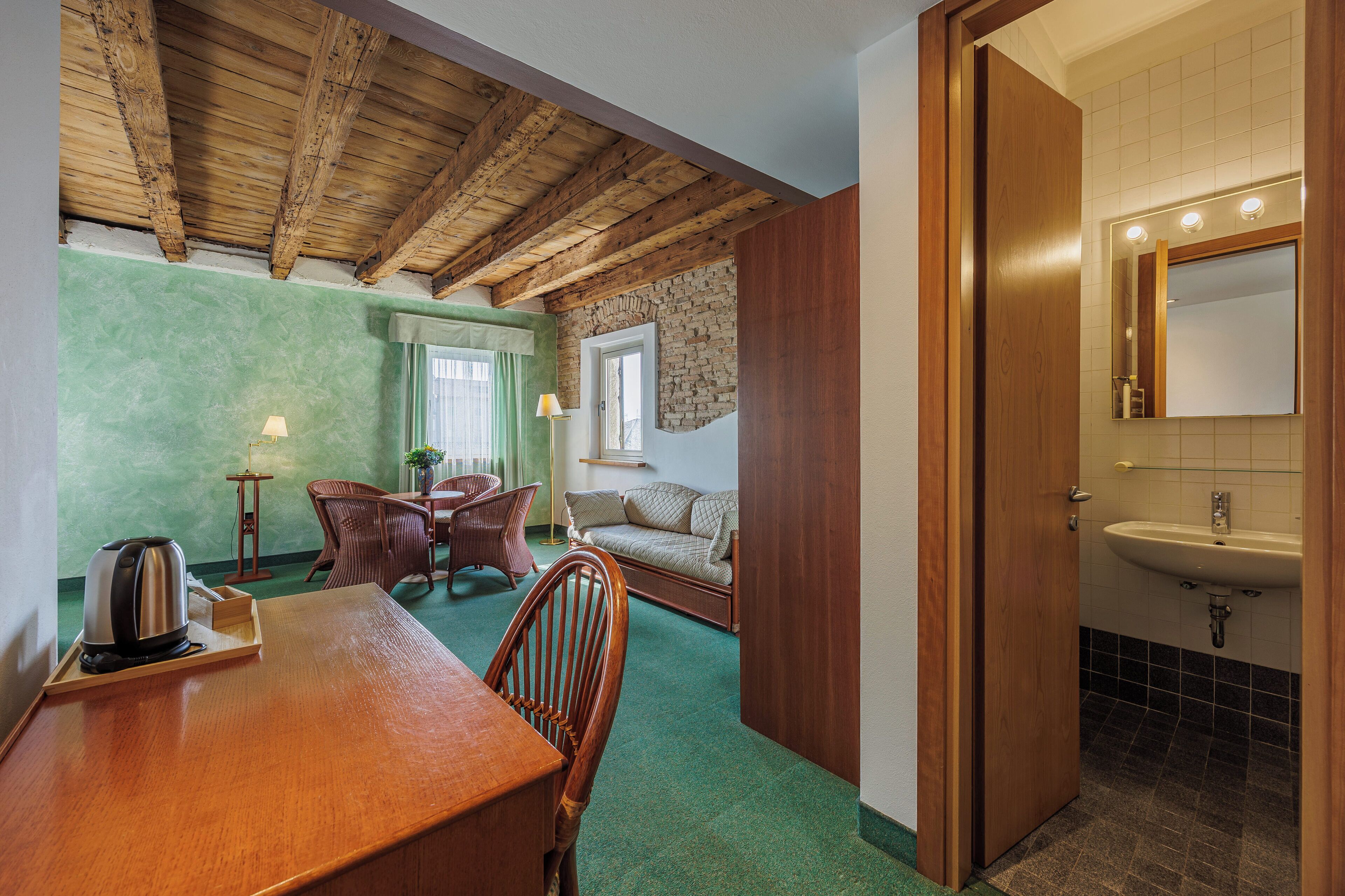 Una habitación con techo de madera, un área de comedor con una mesa y sillas, un sofá, un ventanal pequeño y un baño con lavamanos y espejo.