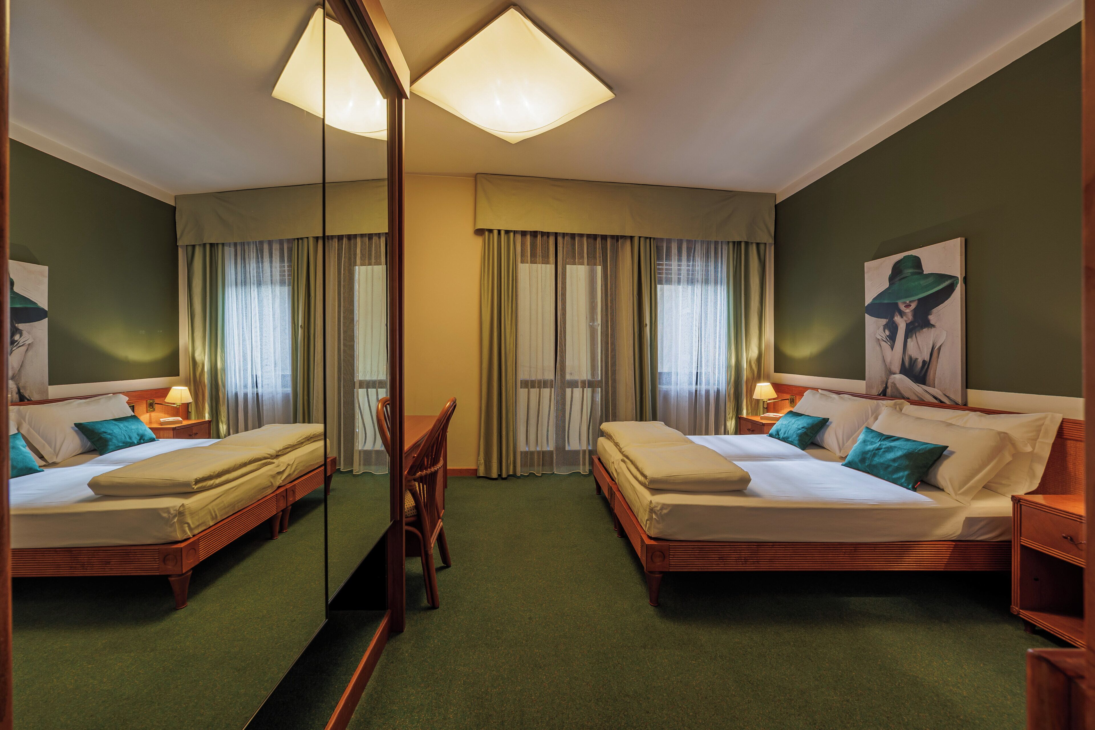 A hotel room with two beds, a desk, a chair, a mirror, and a painting on the wall.
