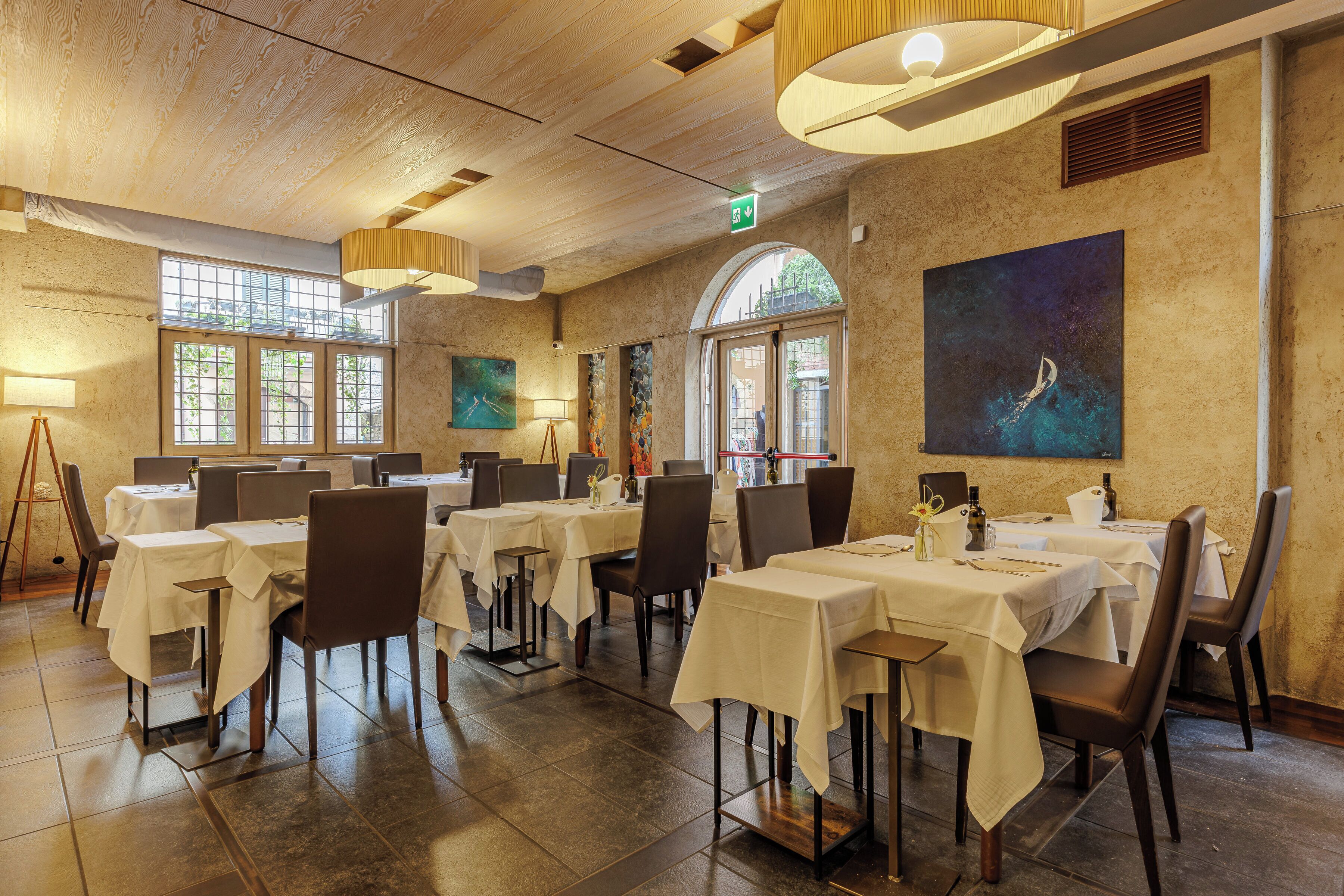 Ein Restaurant mit mehreren Tischen und Stühlen, großen Fenstern und einem Bild an der Wand.