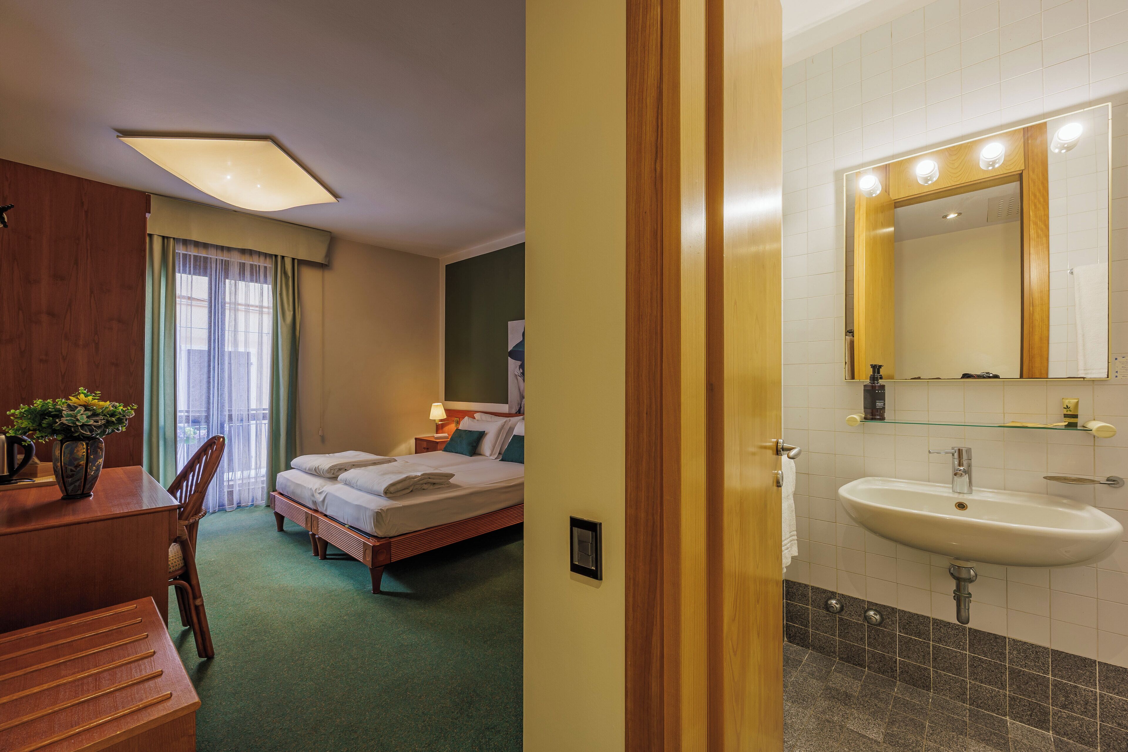 A hotel room with a bed, bedside table, lamp, and a bathroom with a sink and mirror.