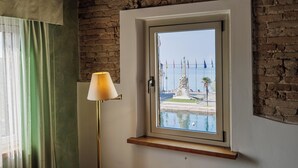 Una habitación con ventana que da a una piscina, banderas y una estatua.