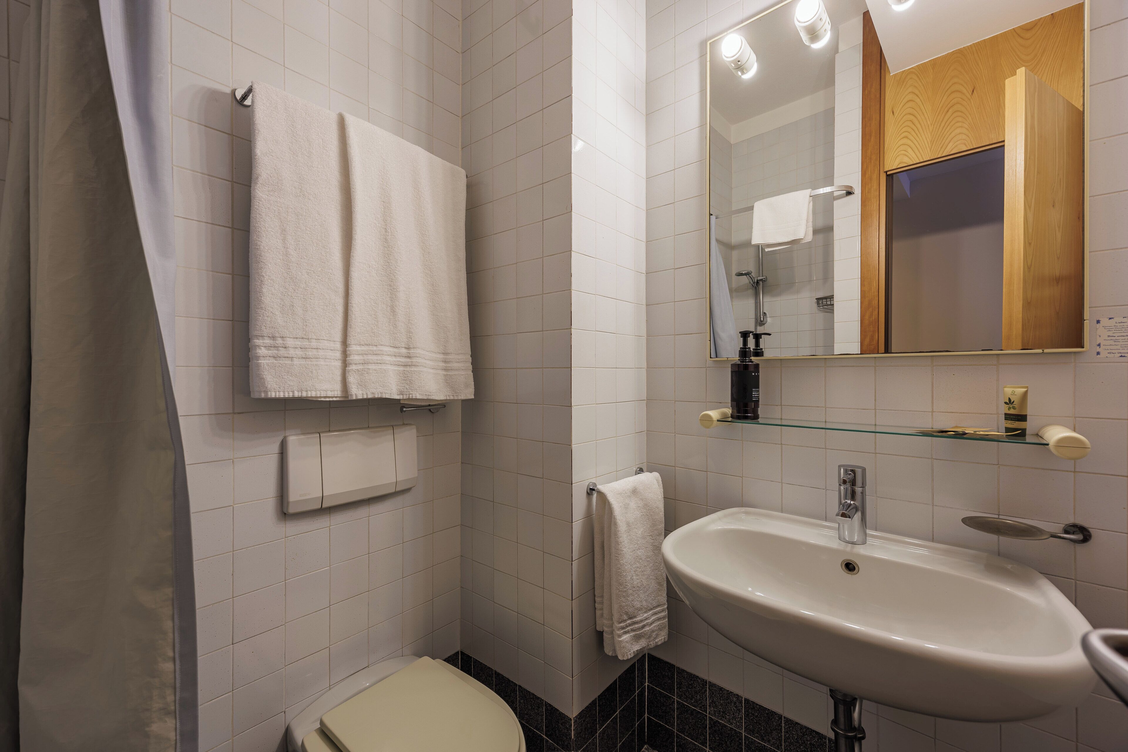 Un baño con inodoro, lavamanos, espejo y toallero.