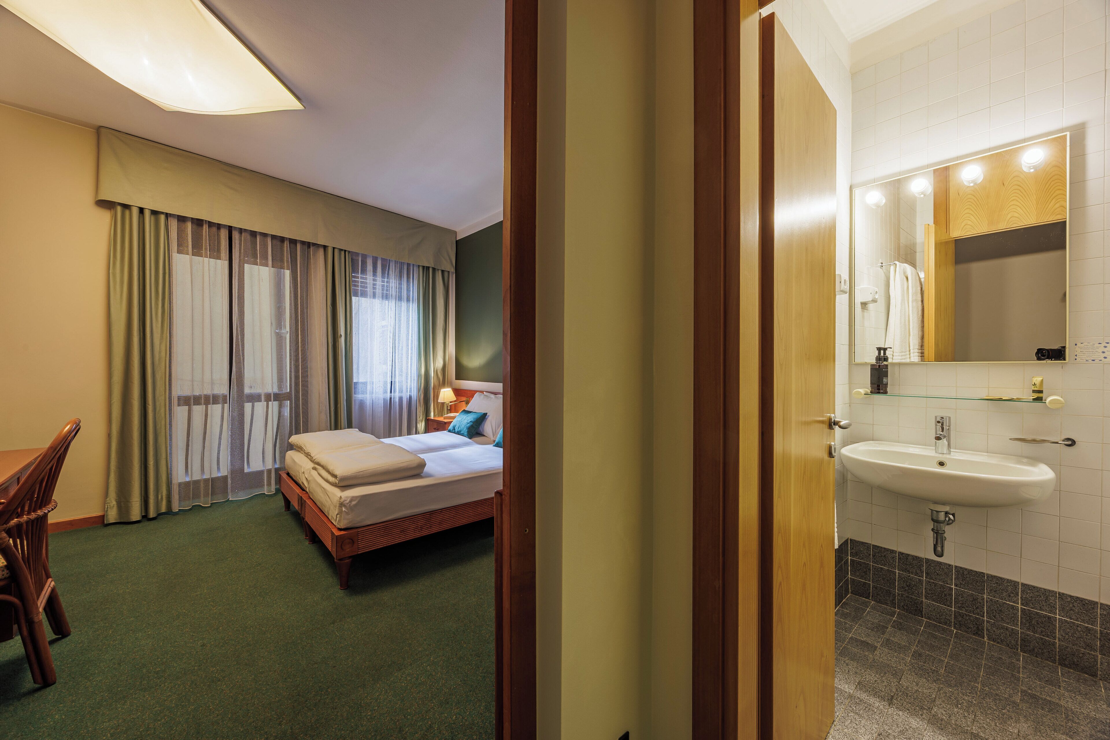 Una habitación de hotel con cama, escritorio, silla y baño con lavamanos y espejo.