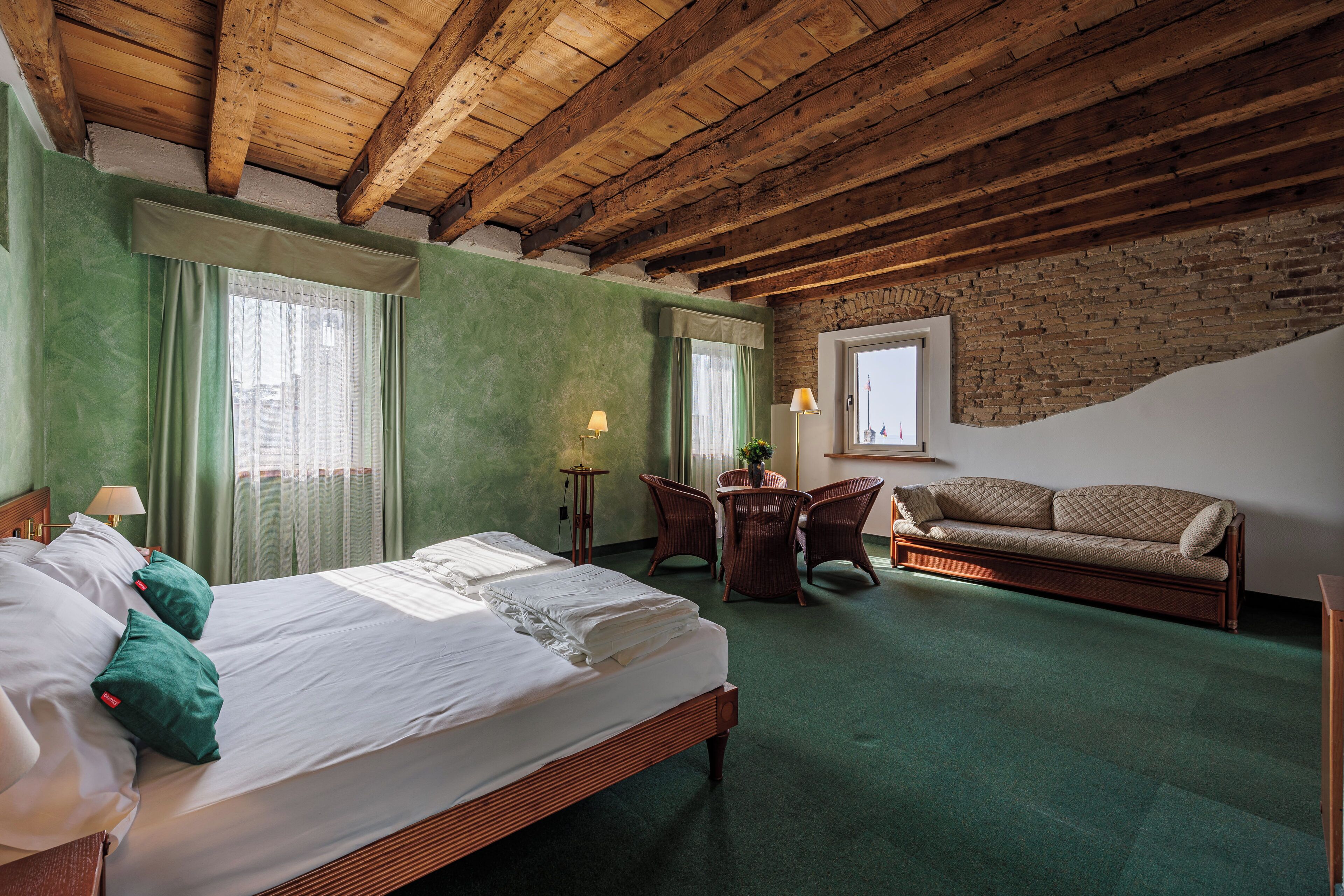 A hotel room with a large bed, a sofa, a small table, and a chair.