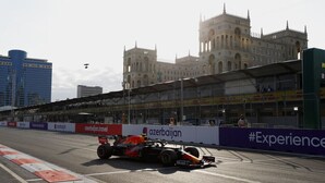 Een Formule 1-auto op een racecircuit met een imposant gebouw op de achtergrond.