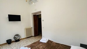 Un dormitorio con una cama, un televisor de pantalla plana, un ventilador de techo y un radiador.