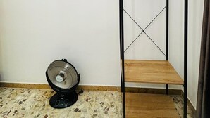 Una habitación con una televisión montada en la pared, un ventilador de pie y una estantería de madera.