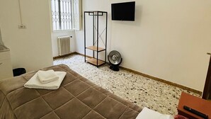 Un dormitorio con cama, televisor, radiador y ventana con rejas.